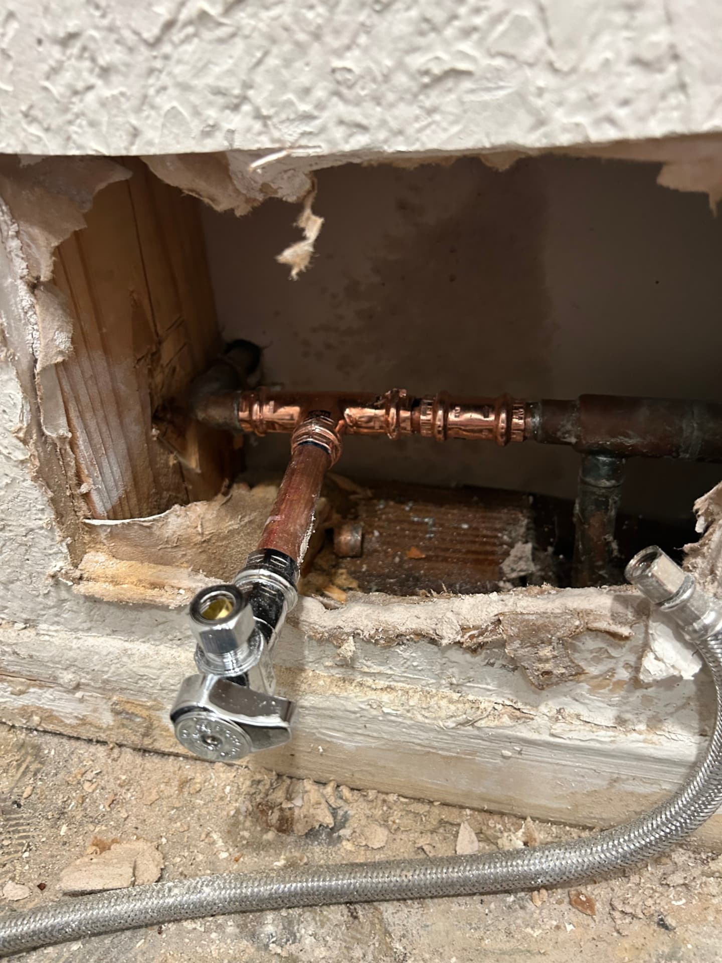 Open wall showing a replaced section of copper pipe with a new chrome angle stop valve installed