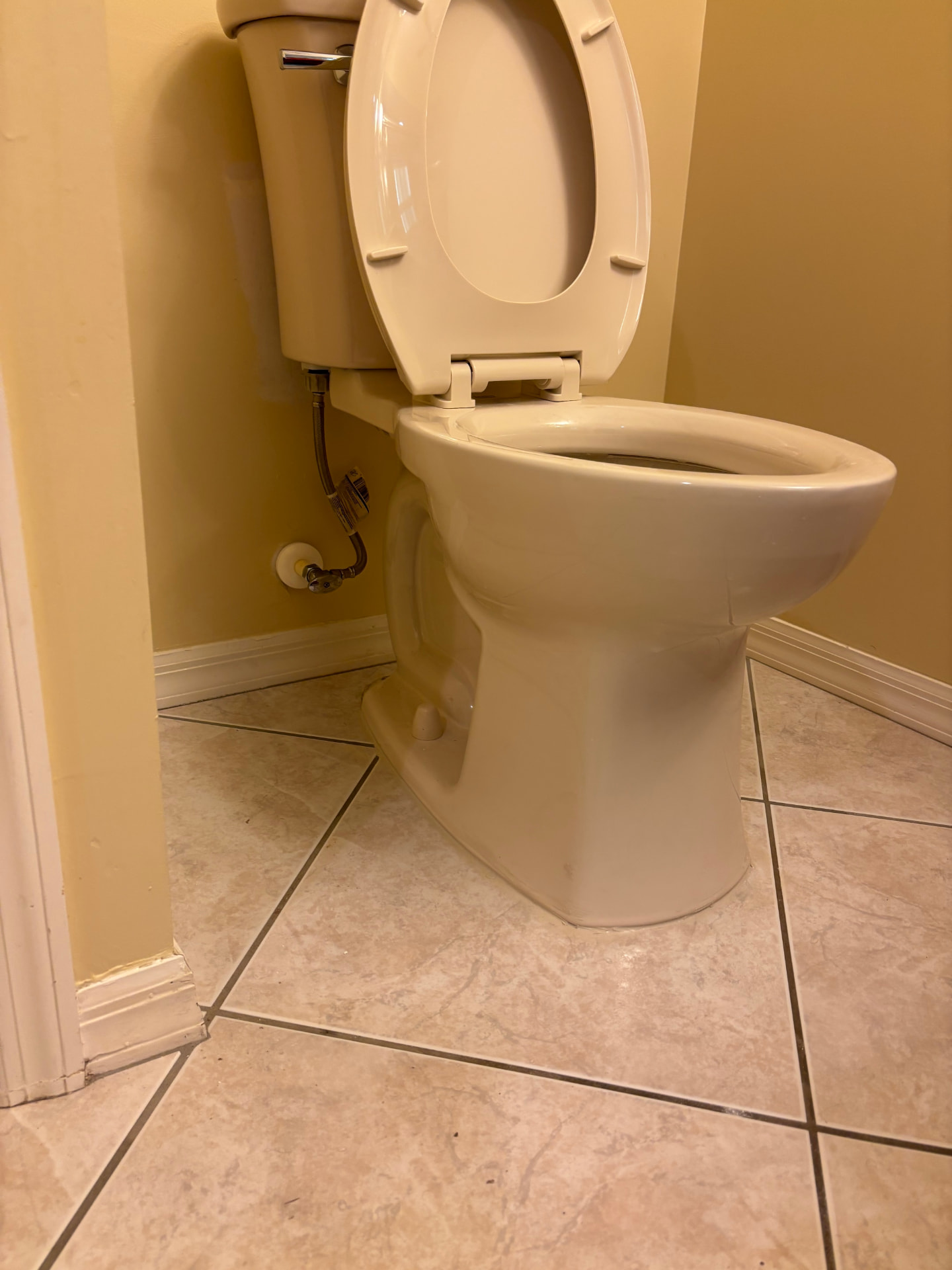Newly installed bone-color toilet connected with a braided stainless supply line and chrome angle stop shutoff