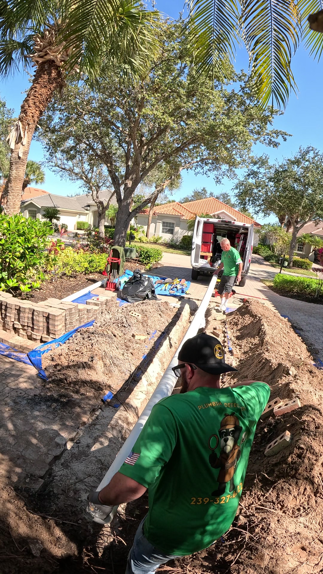 Crew lowering a new PVC sewer line into an open yard trench after cutting out the root-damaged section