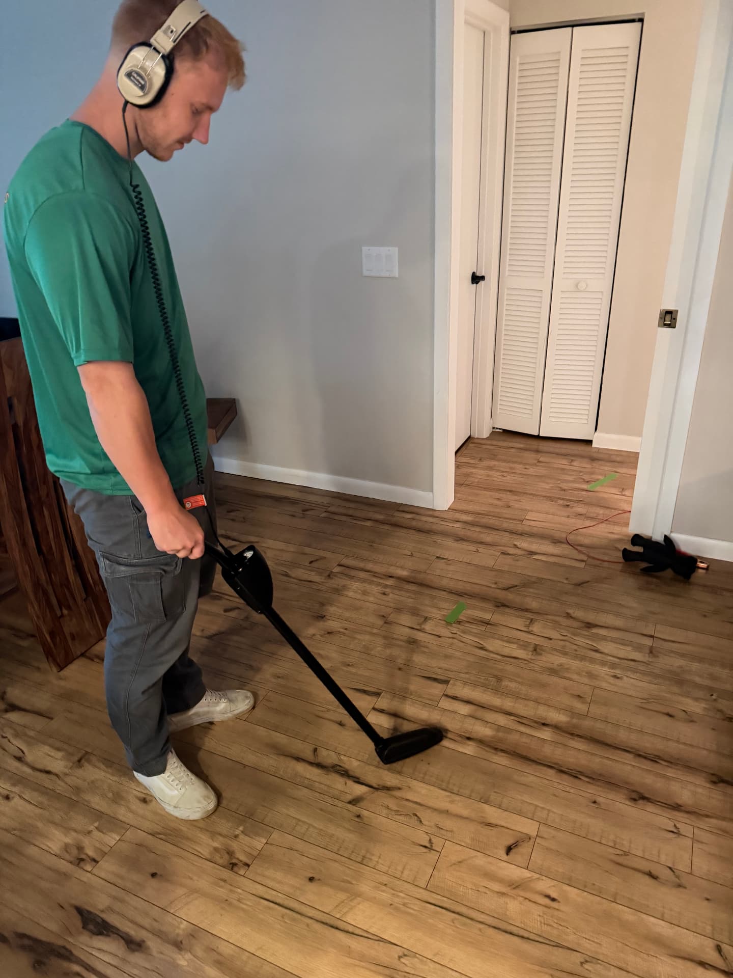 Technician scanning a wood floor with acoustic listening equipment, marking the traced water line with tape