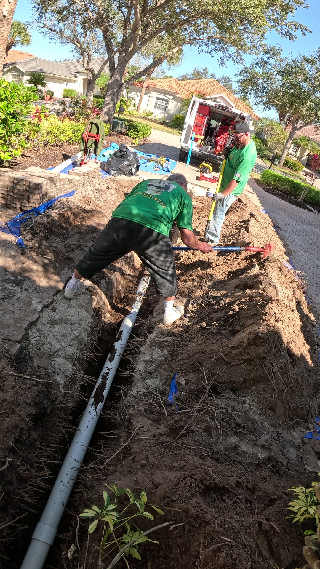 Two Plumbing Detectives technicians hand-backfilling a yard trench over a newly replaced PVC sewer line
