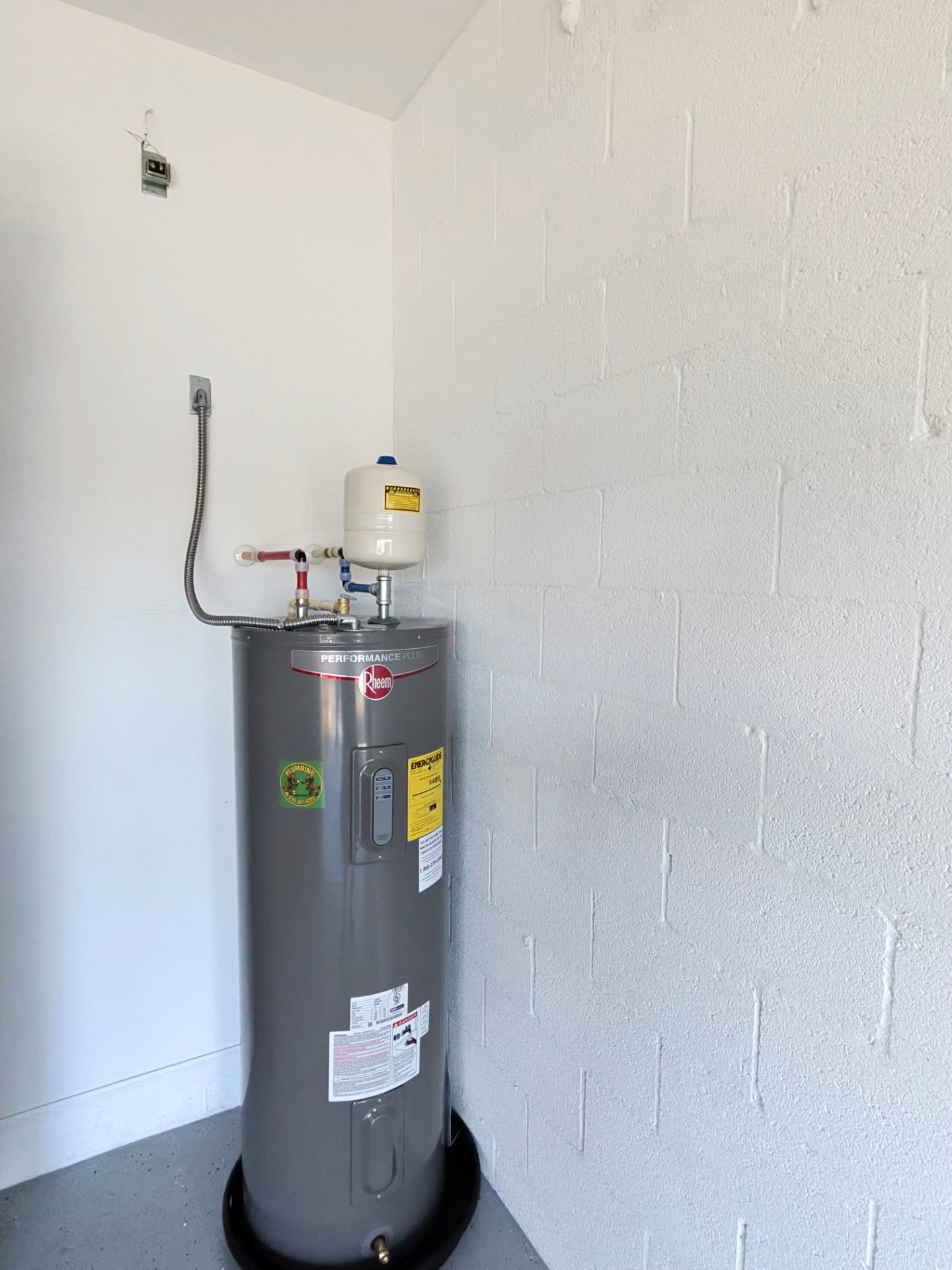 Rheem Performance Plus water heater installed in a garage corner with expansion tank, brass shutoff, and drain pan