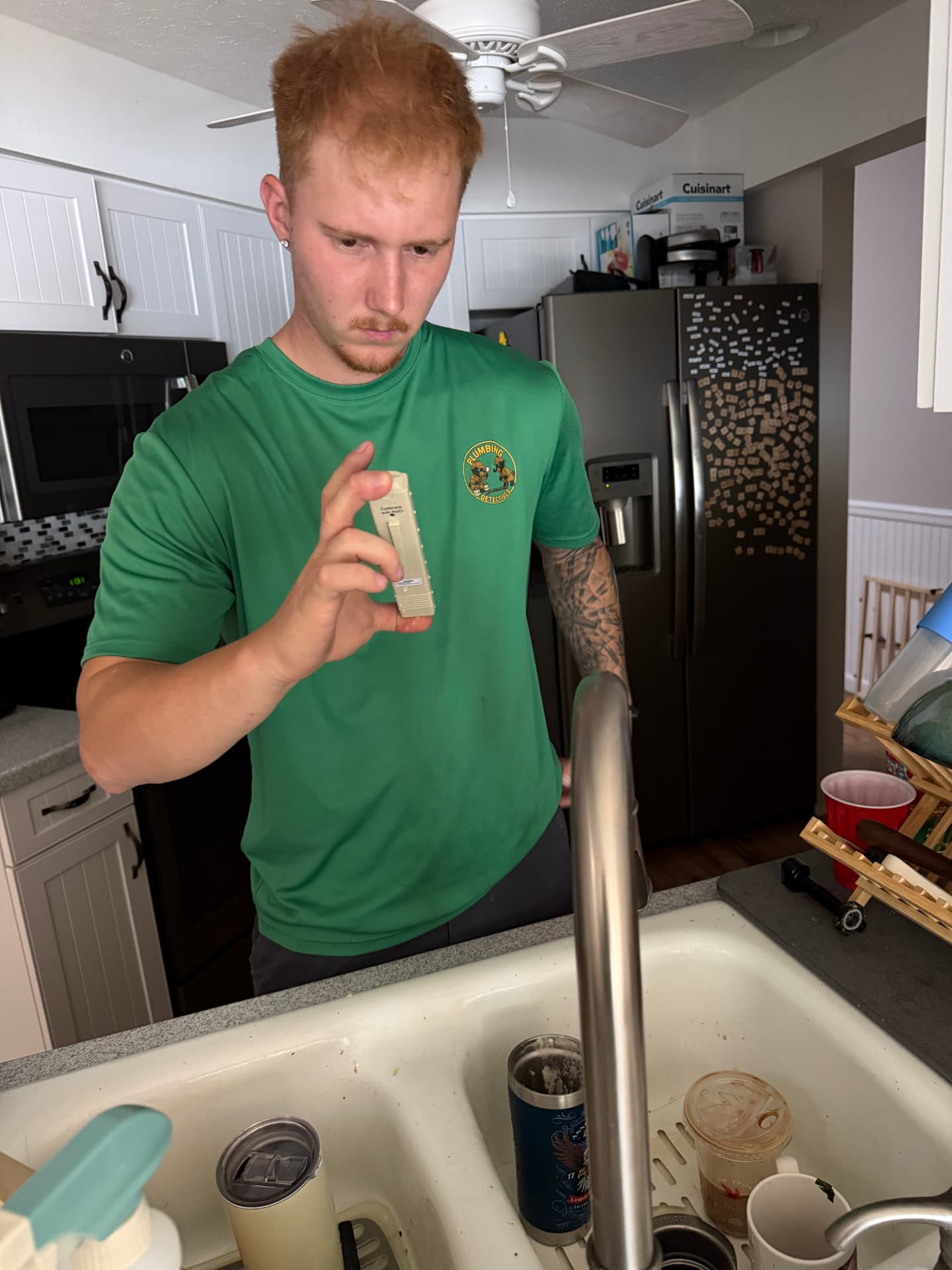 Plumbing Detectives technician reading a handheld water test meter at a kitchen faucet