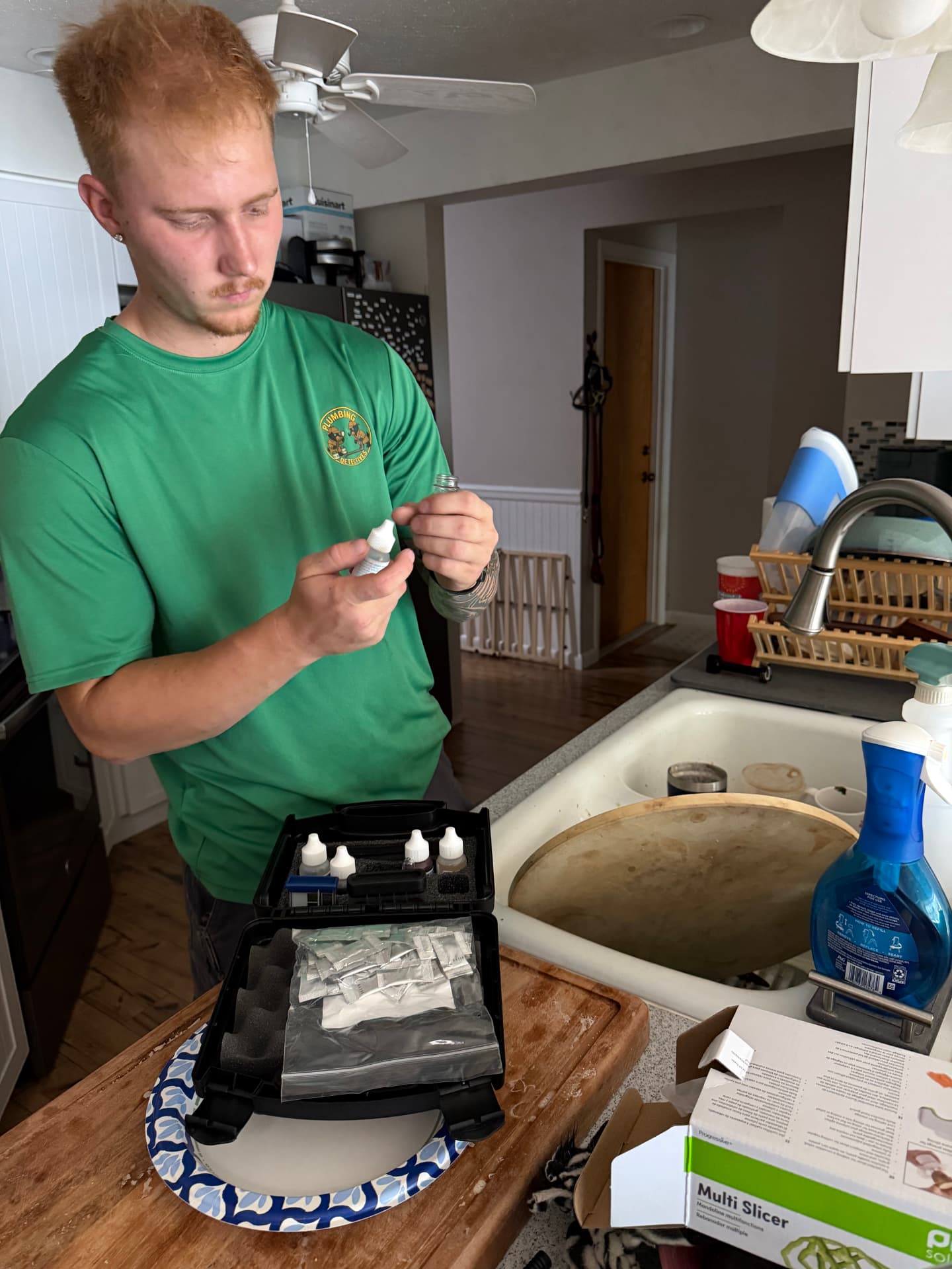 Plumbing Detectives technician preparing reagents from an open water test kit beside a kitchen sink