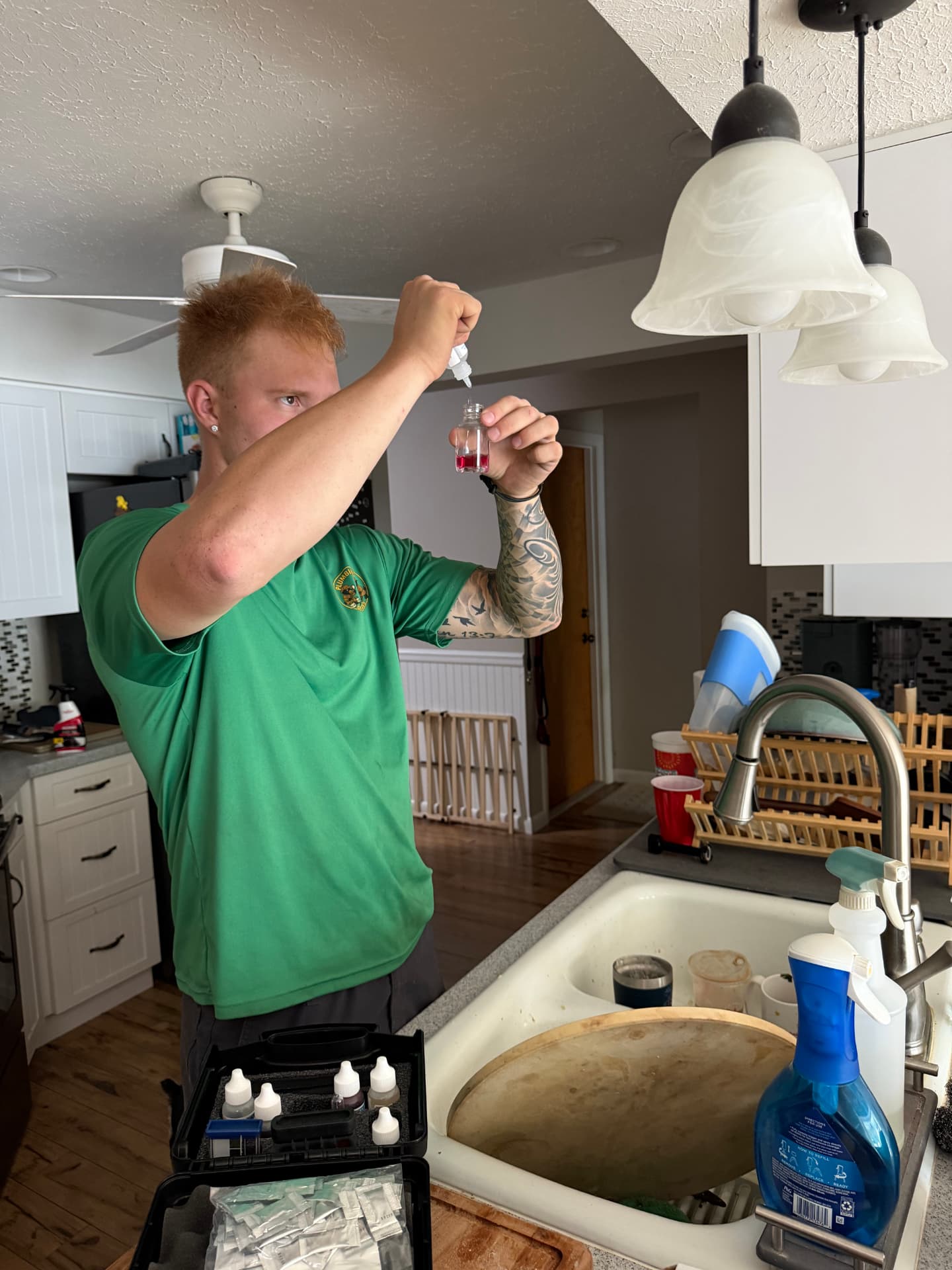 Plumbing Detectives technician adding reagent drops to a water sample for a hardness test at a kitchen sink