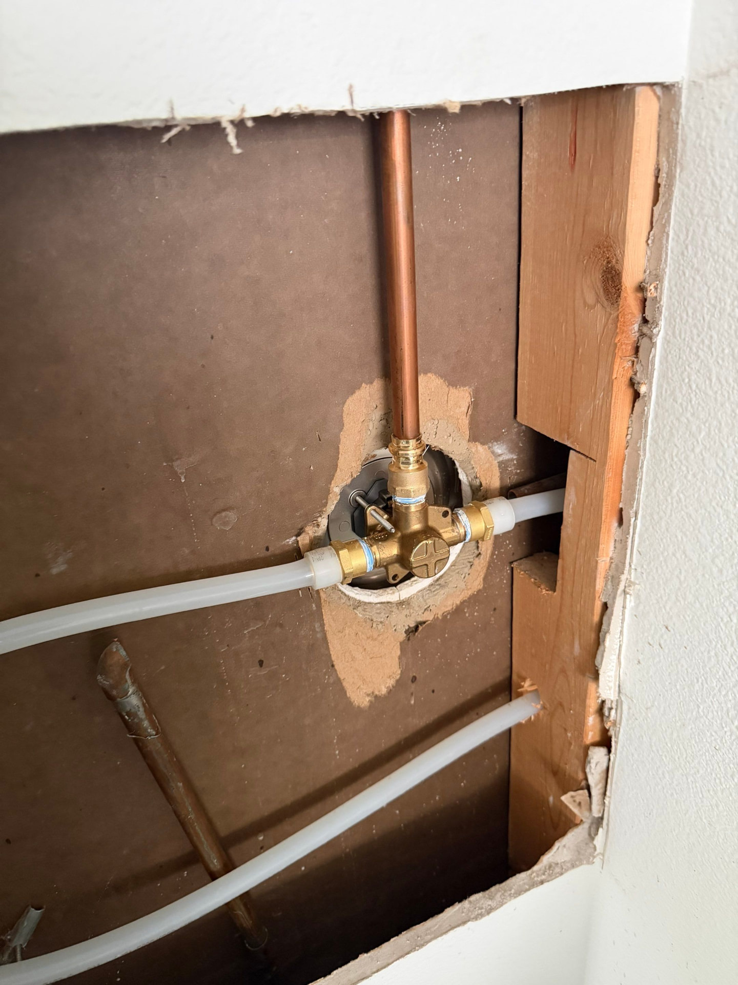 Small drywall access opening at a shower valve with abandoned copper piping and new PEX supply lines