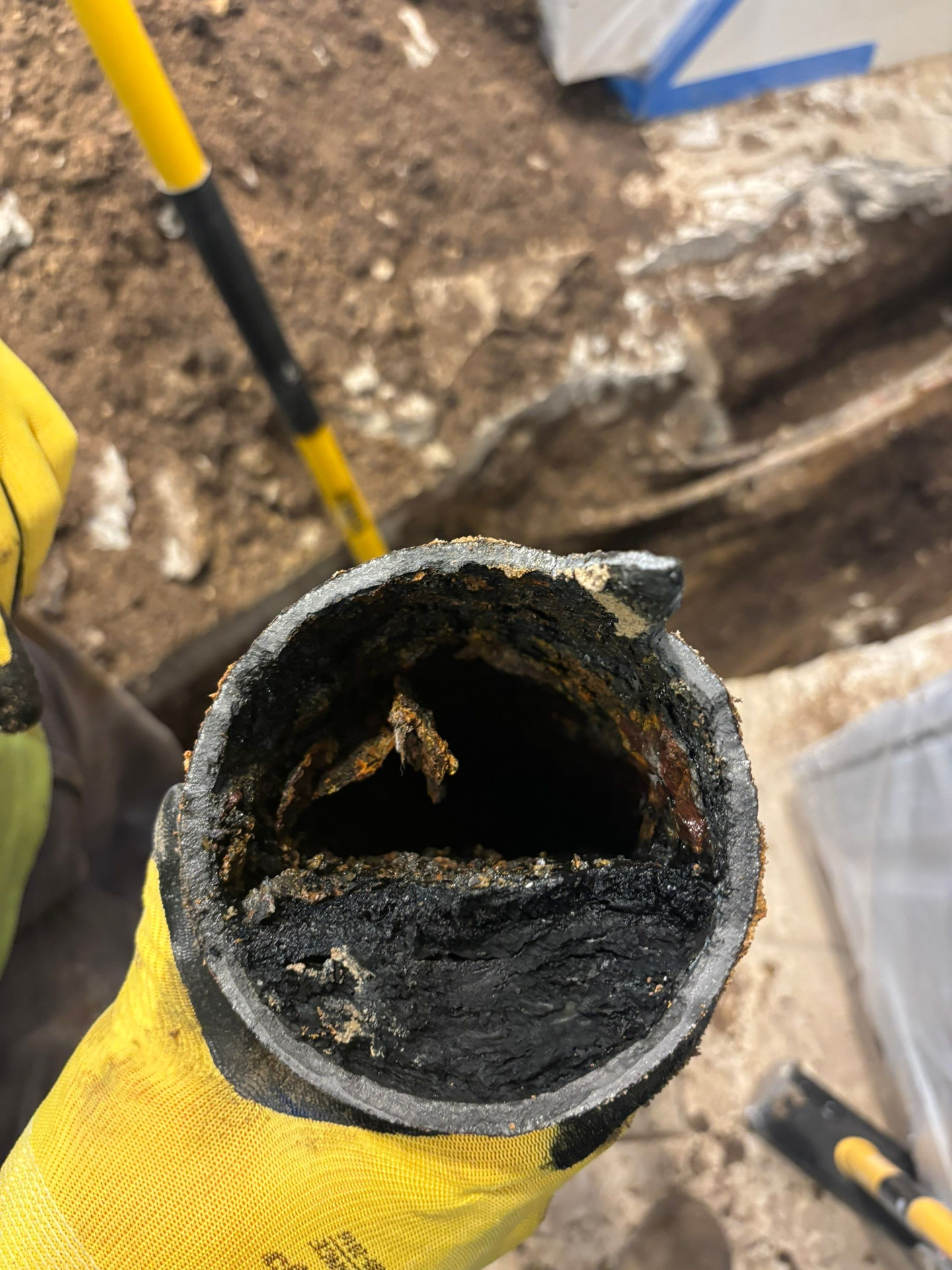 Inside of a removed cast-iron sewer pipe showing heavy soot, scale, and decay narrowing the line