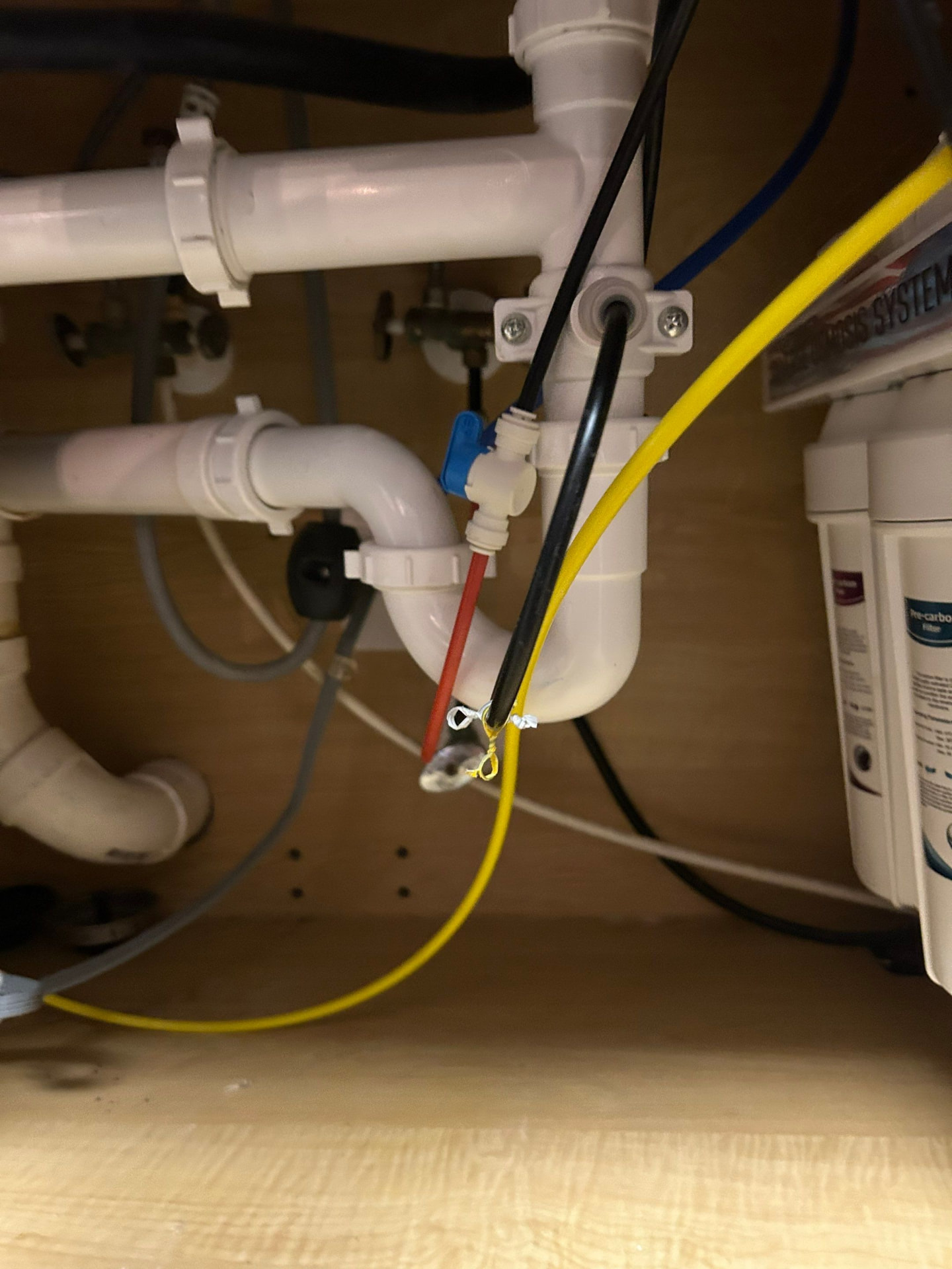 Reverse osmosis tank valve and drain connection with color-coded tubing under a kitchen sink