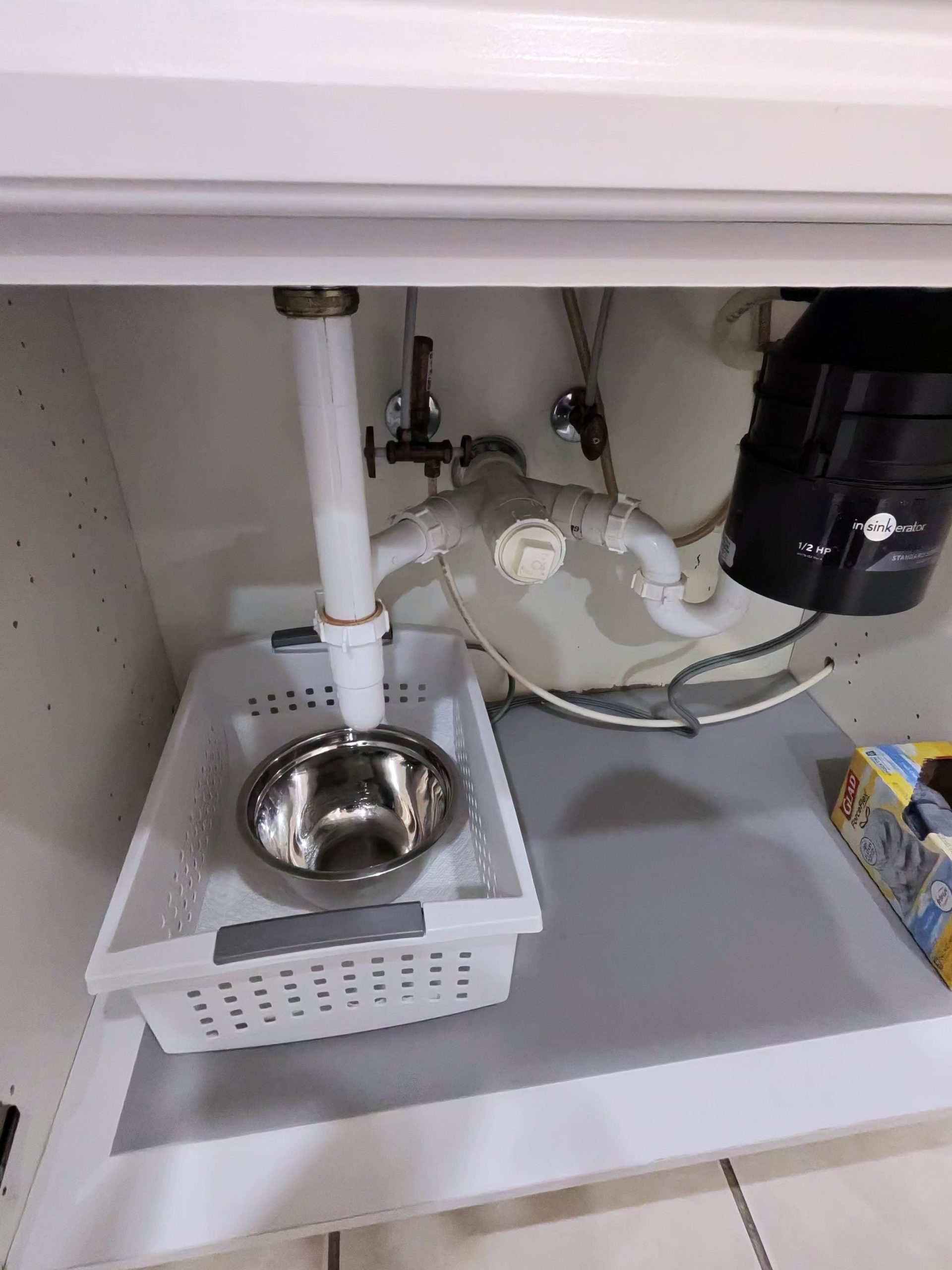 Under-sink plumbing with pipes, garbage disposal, and a small metal bowl.